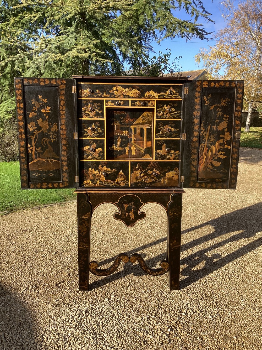 A Regency period black lacquer cabinet on stand, featuring gilt Chinoiserie landscape and floral scenes, open double doors, and fitted internal drawers surrounding a central panel.