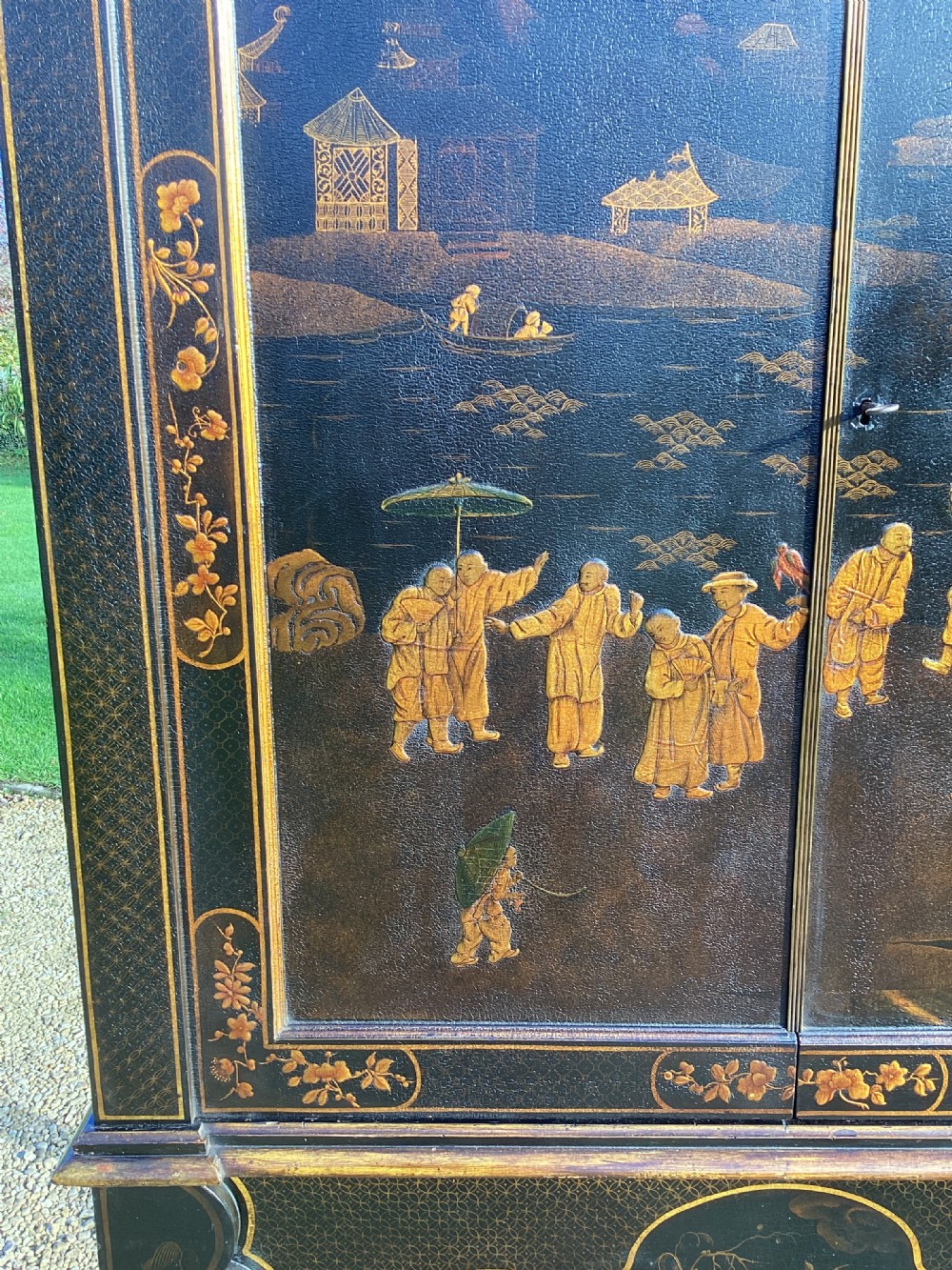 A Regency period black lacquer cabinet on stand, featuring gilt Chinoiserie landscape and floral scenes, open double doors, and fitted internal drawers surrounding a central panel. View II