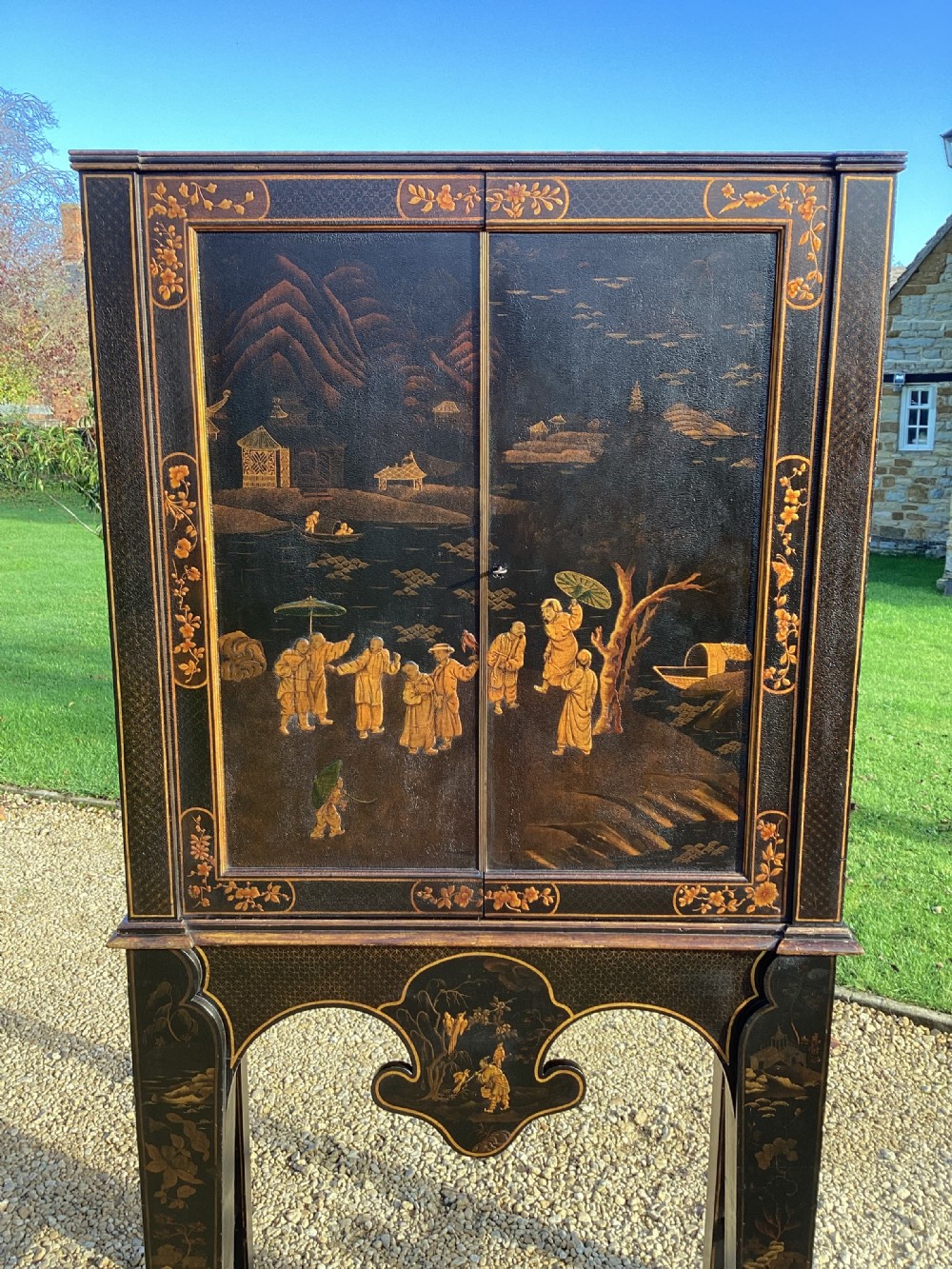 A Regency period black lacquer cabinet on stand, featuring gilt Chinoiserie landscape and floral scenes, open double doors, and fitted internal drawers surrounding a central panel. View III