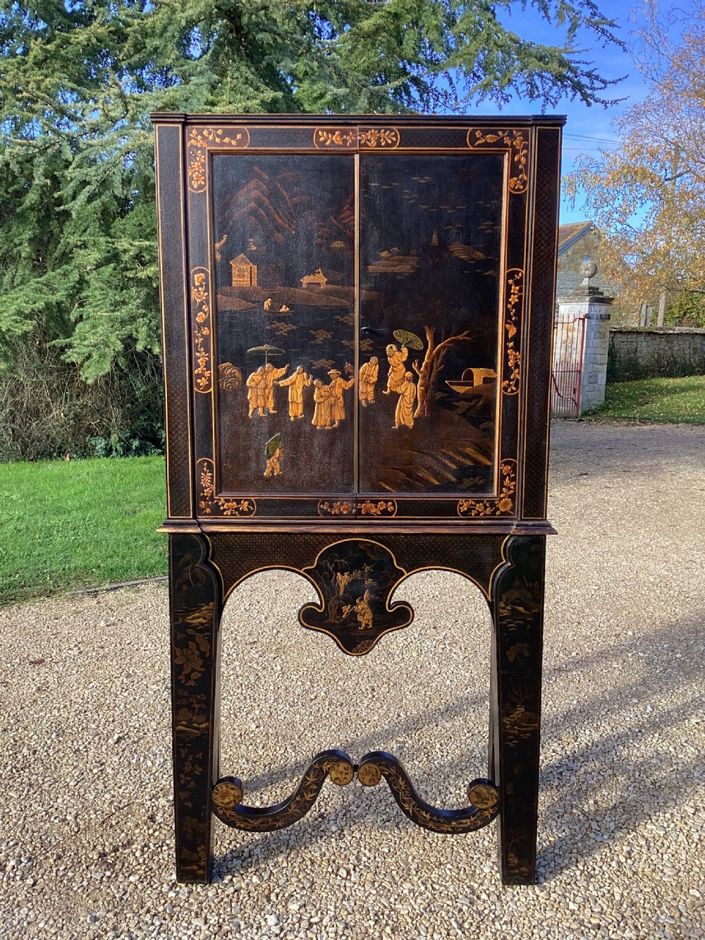 A Regency period black lacquer cabinet on stand, featuring gilt Chinoiserie landscape and floral scenes, open double doors, and fitted internal drawers surrounding a central panel. View V