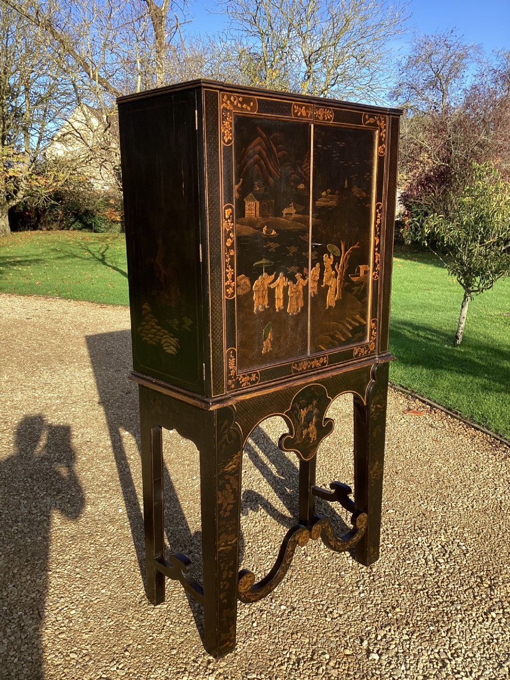 A Regency period black lacquer cabinet on stand, featuring gilt Chinoiserie landscape and floral scenes, open double doors, and fitted internal drawers surrounding a central panel. View VI