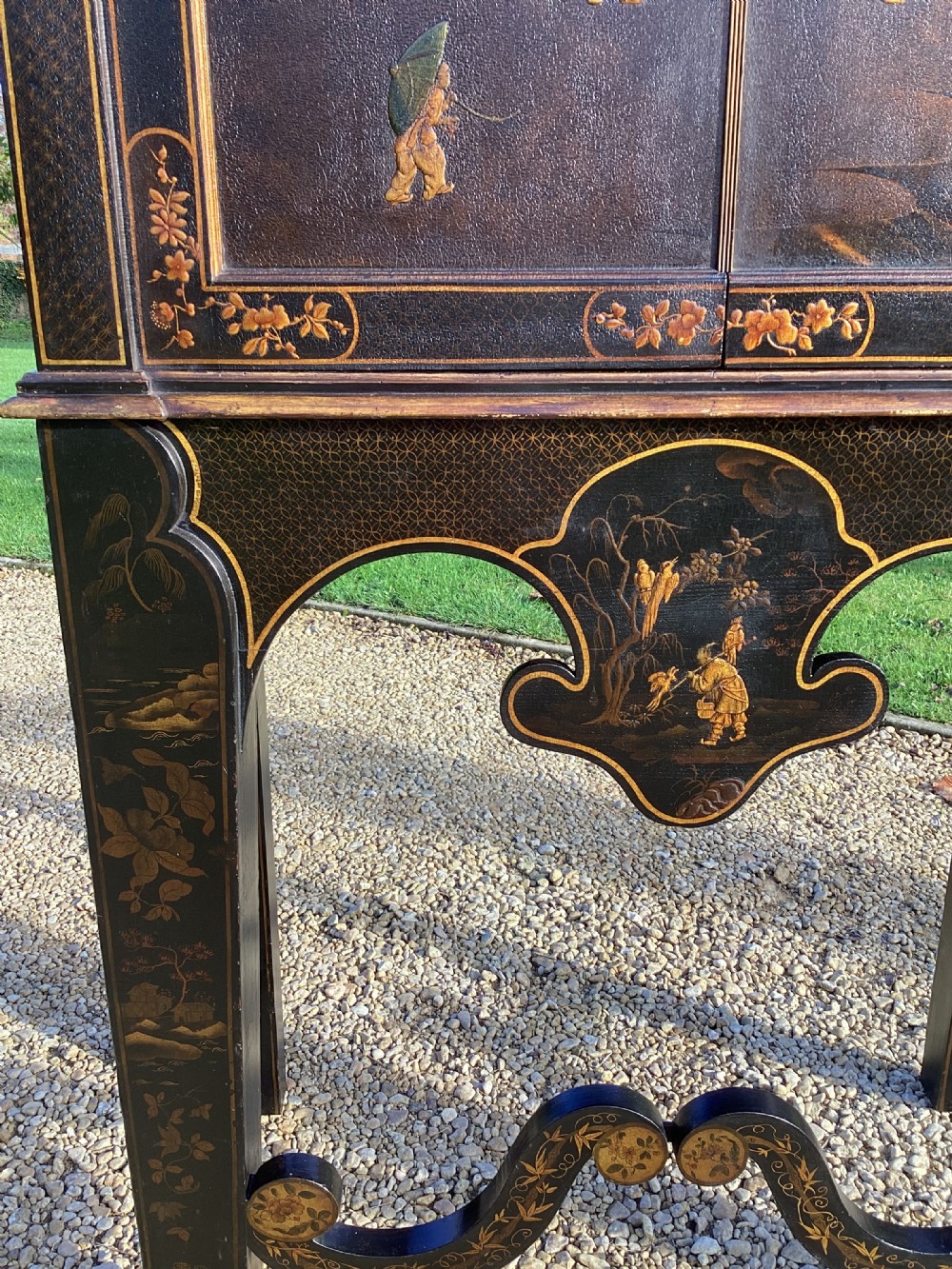 A Regency period black lacquer cabinet on stand, featuring gilt Chinoiserie landscape and floral scenes, open double doors, and fitted internal drawers surrounding a central panel. View VII
