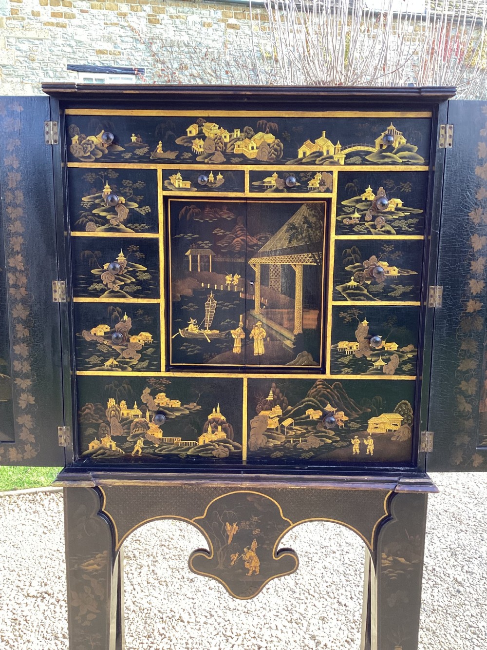 A Regency period black lacquer cabinet on stand, featuring gilt Chinoiserie landscape and floral scenes, open double doors, and fitted internal drawers surrounding a central panel. View XI
