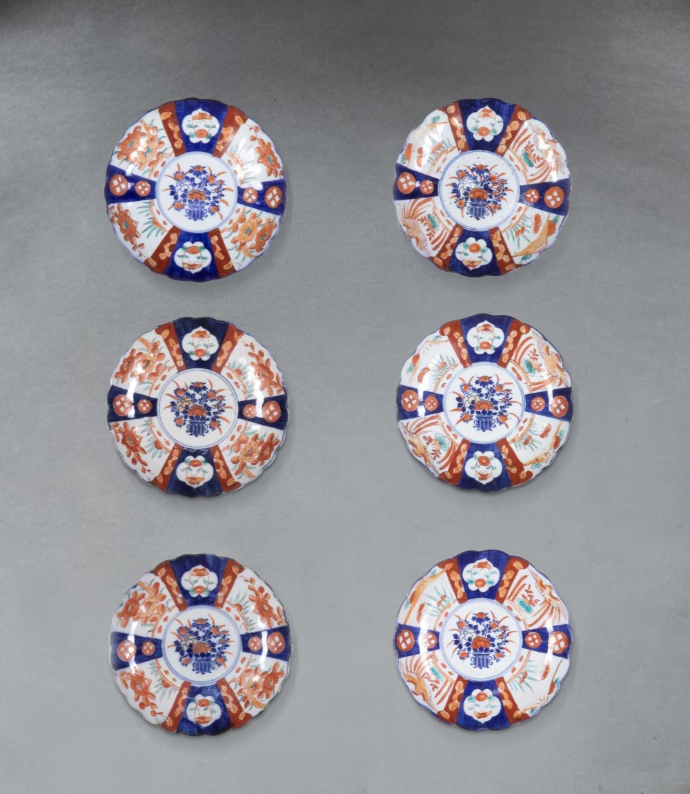 A set of six late nineteenth-century Japanese Imari porcelain plates featuring scalloped edges, central floral medallions, and panelled borders in cobalt blue and iron red.