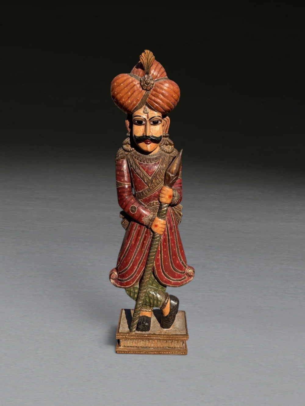 A 19th-century carved and painted wooden figure of an Indian soldier standing on a rectangular base holding a spear.