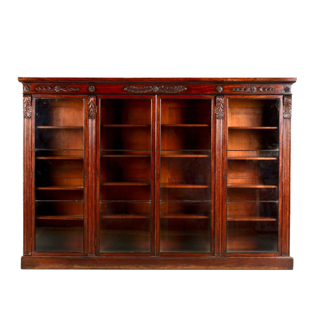A matching pair of low, broad Regency mahogany bookcases featuring four glazed doors, carved upper friezes, and plinth bases. View II