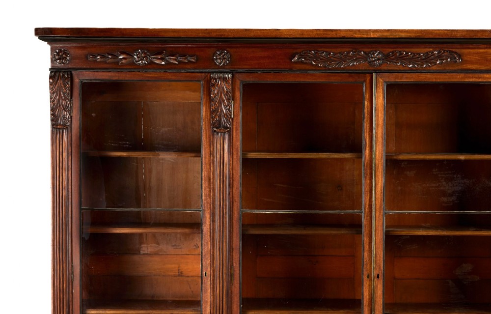 A matching pair of low, broad Regency mahogany bookcases featuring four glazed doors, carved upper friezes, and plinth bases. View V