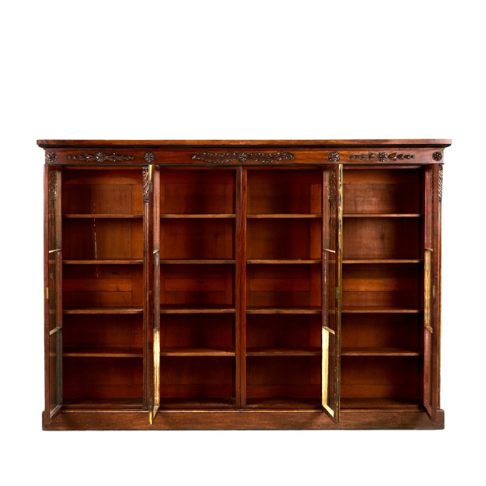 A matching pair of low, broad Regency mahogany bookcases featuring four glazed doors, carved upper friezes, and plinth bases. View VI