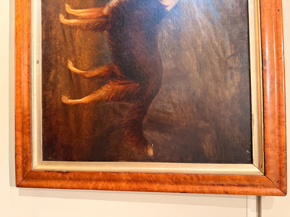 A 19th-century primitive oil painting on canvas depicting a standing brown and white dog set against a landscape backdrop, housed within a wide wood frame. View II