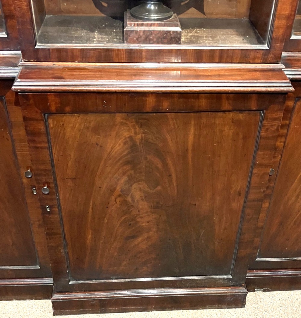 A Georgian flame mahogany breakfront bookcase featuring glazed upper doors and panelled lower cupboard doors. View IV