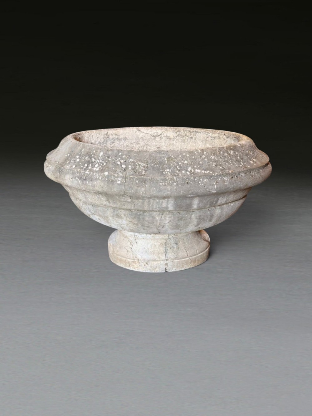 A hand-carved 18th-century grey marble cistern featuring a wide moulded rim and a heavy circular pedestal base.