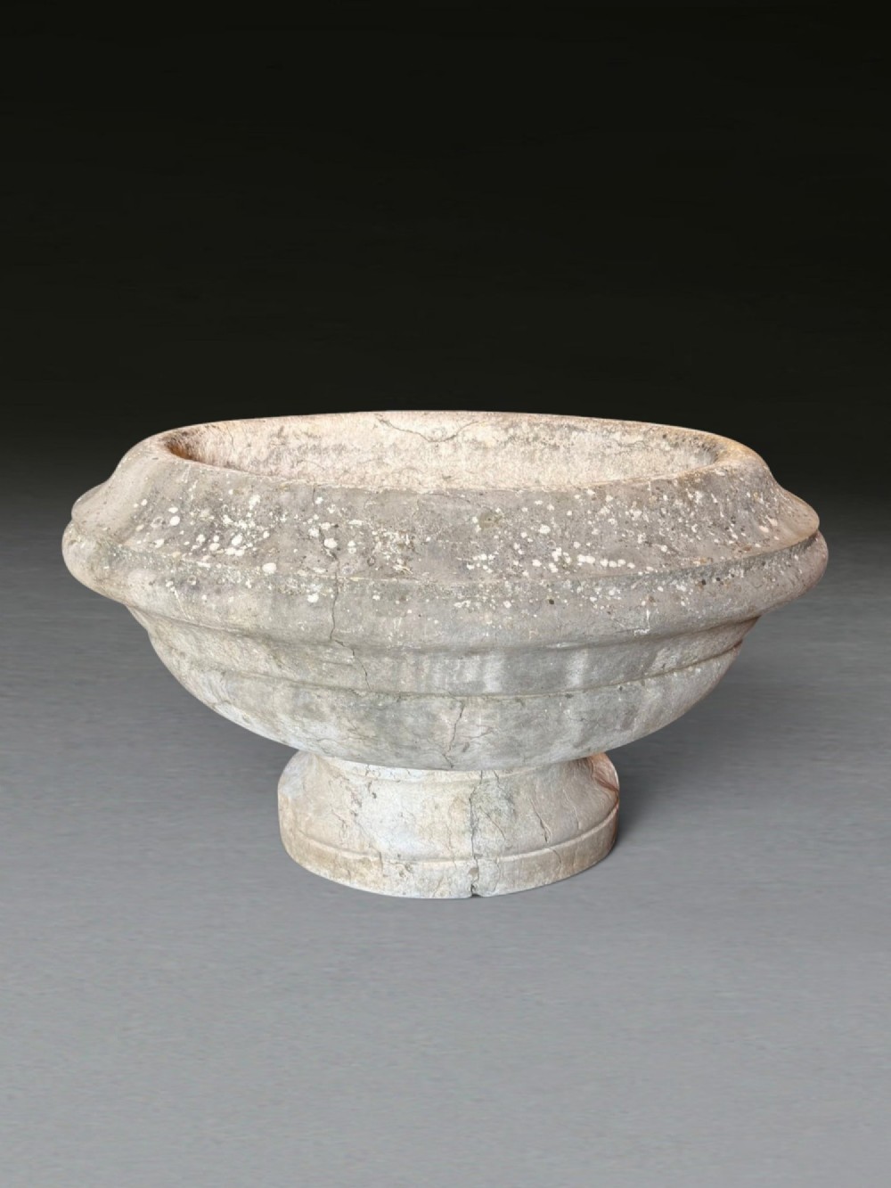 A hand-carved 18th-century grey marble cistern featuring a wide moulded rim and a heavy circular pedestal base. View II