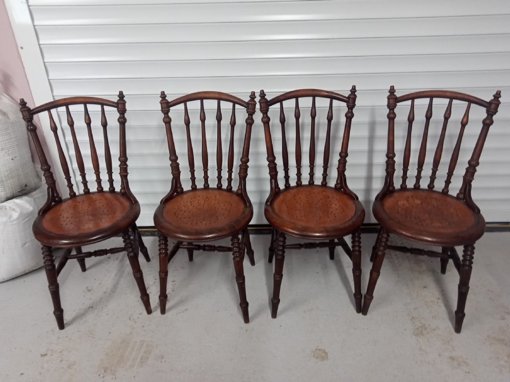 A set of four dark brown Edwardian wooden cafe chairs featuring spindle backs, turned legs, and circular seats with perforated dot patterns.
