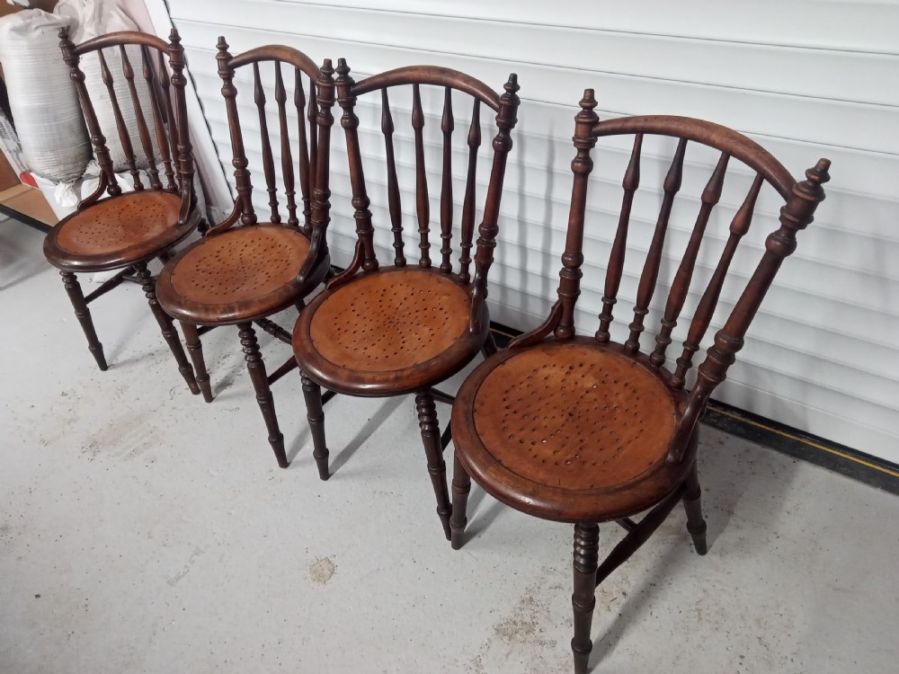 A set of four dark brown Edwardian wooden cafe chairs featuring spindle backs, turned legs, and circular seats with perforated dot patterns. View II