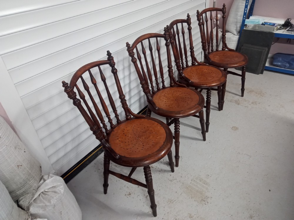 A set of four dark brown Edwardian wooden cafe chairs featuring spindle backs, turned legs, and circular seats with perforated dot patterns. View III