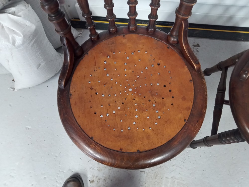 A set of four dark brown Edwardian wooden cafe chairs featuring spindle backs, turned legs, and circular seats with perforated dot patterns. View IV