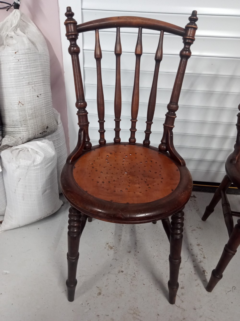 A set of four dark brown Edwardian wooden cafe chairs featuring spindle backs, turned legs, and circular seats with perforated dot patterns. View V