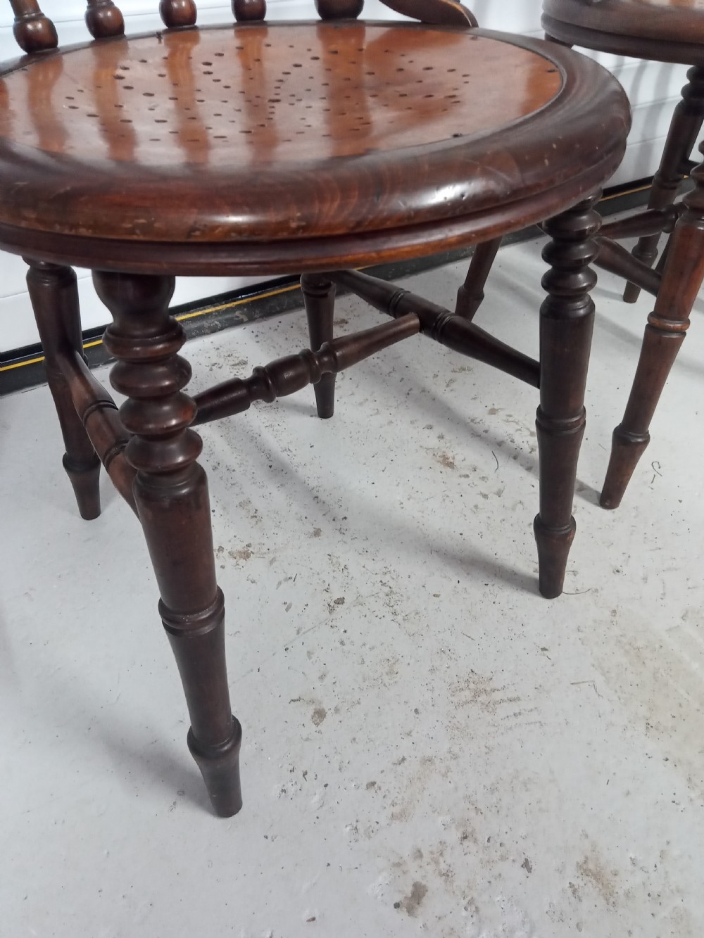 A set of four dark brown Edwardian wooden cafe chairs featuring spindle backs, turned legs, and circular seats with perforated dot patterns. View VIII