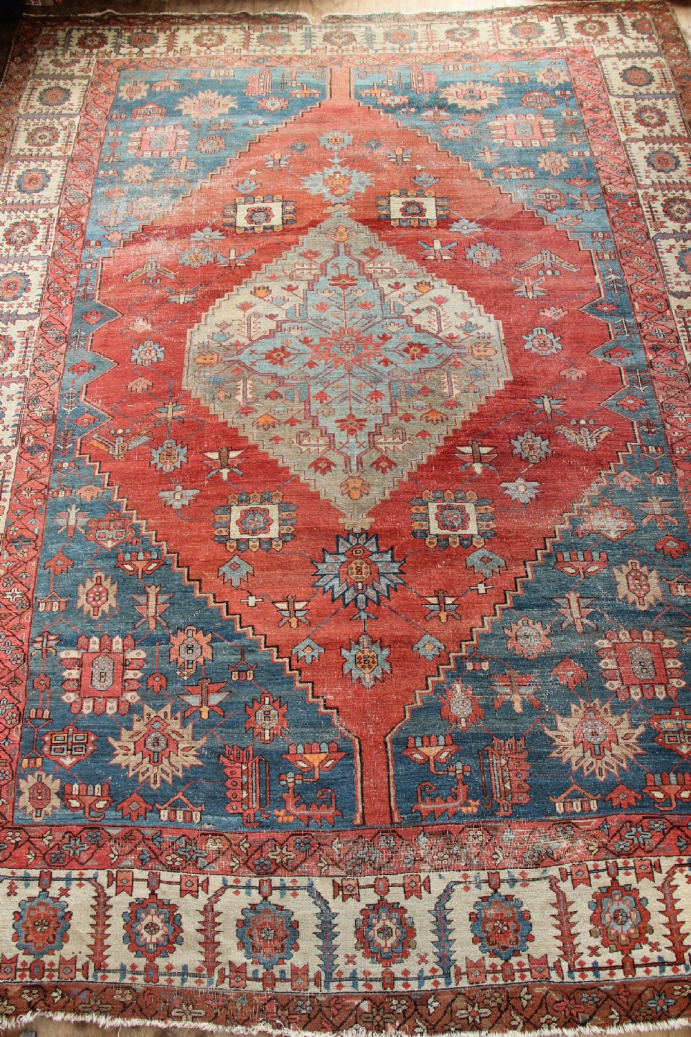 An oversized hand-knotted Persian carpet featuring a central geometric star medallion in light blue and cream on a terracotta field with blue spandrels and patterned borders.
