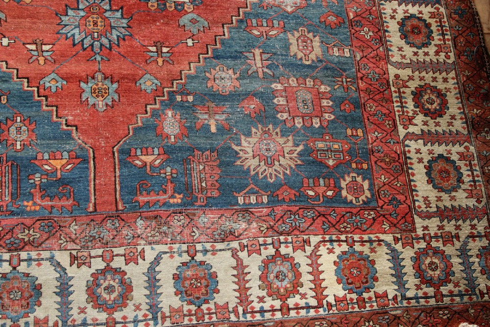 An oversized hand-knotted Persian carpet featuring a central geometric star medallion in light blue and cream on a terracotta field with blue spandrels and patterned borders. View V