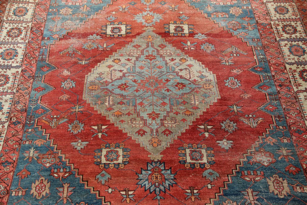An oversized hand-knotted Persian carpet featuring a central geometric star medallion in light blue and cream on a terracotta field with blue spandrels and patterned borders. View VI