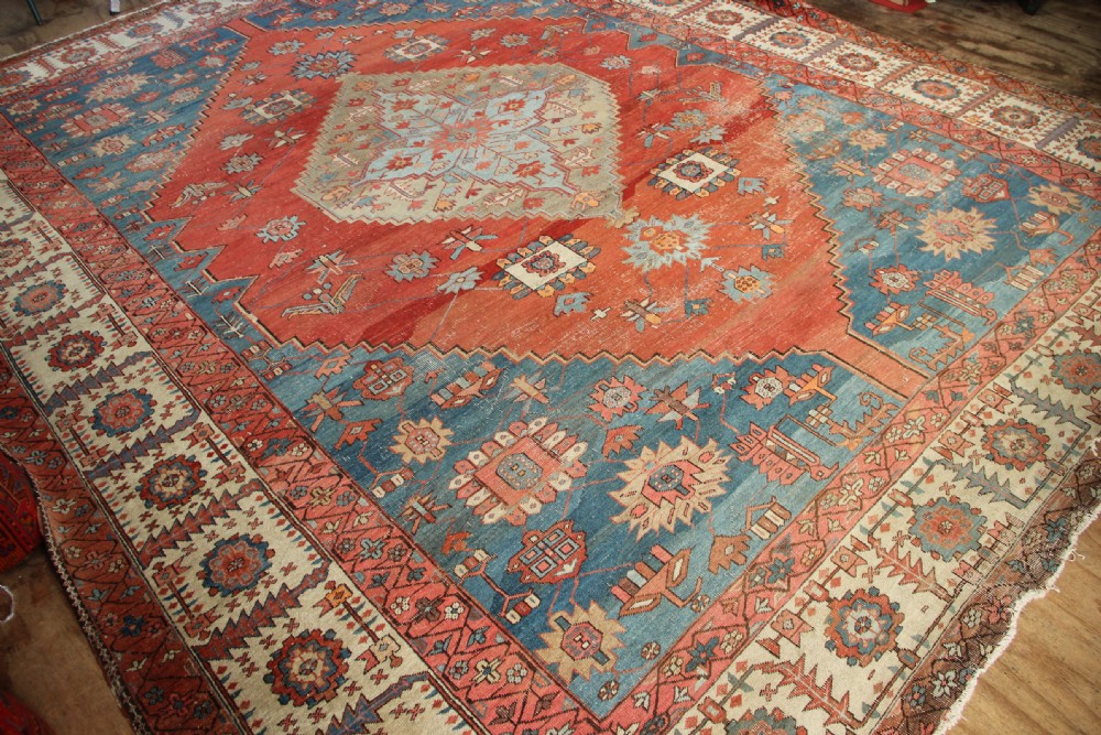 An oversized hand-knotted Persian carpet featuring a central geometric star medallion in light blue and cream on a terracotta field with blue spandrels and patterned borders. View XII