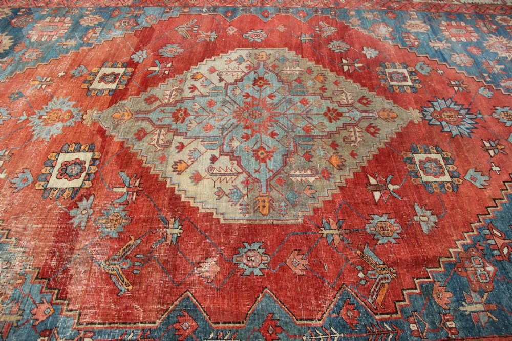 An oversized hand-knotted Persian carpet featuring a central geometric star medallion in light blue and cream on a terracotta field with blue spandrels and patterned borders. View XV