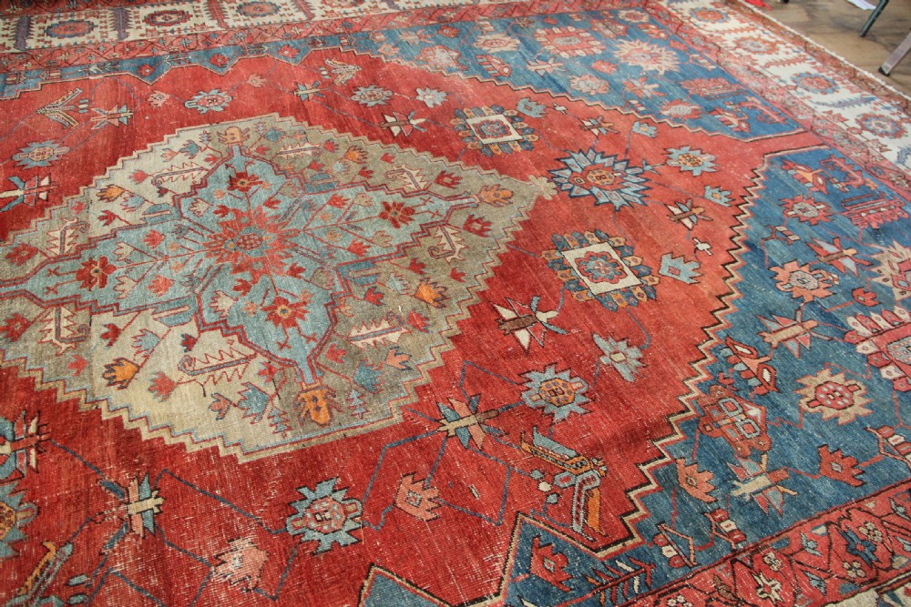 An oversized hand-knotted Persian carpet featuring a central geometric star medallion in light blue and cream on a terracotta field with blue spandrels and patterned borders. View XVI