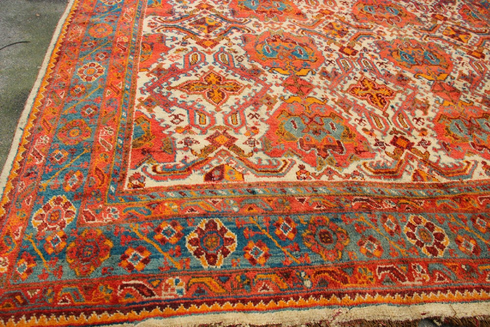 A large hand-knotted wool carpet featuring an ivory field decorated with geometric orange, terracotta, and turquoise medallion motifs within a wide multi-layered border. View II