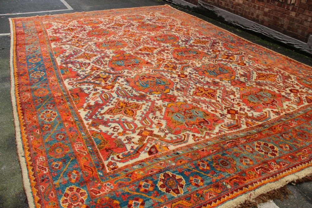 A large hand-knotted wool carpet featuring an ivory field decorated with geometric orange, terracotta, and turquoise medallion motifs within a wide multi-layered border. View III
