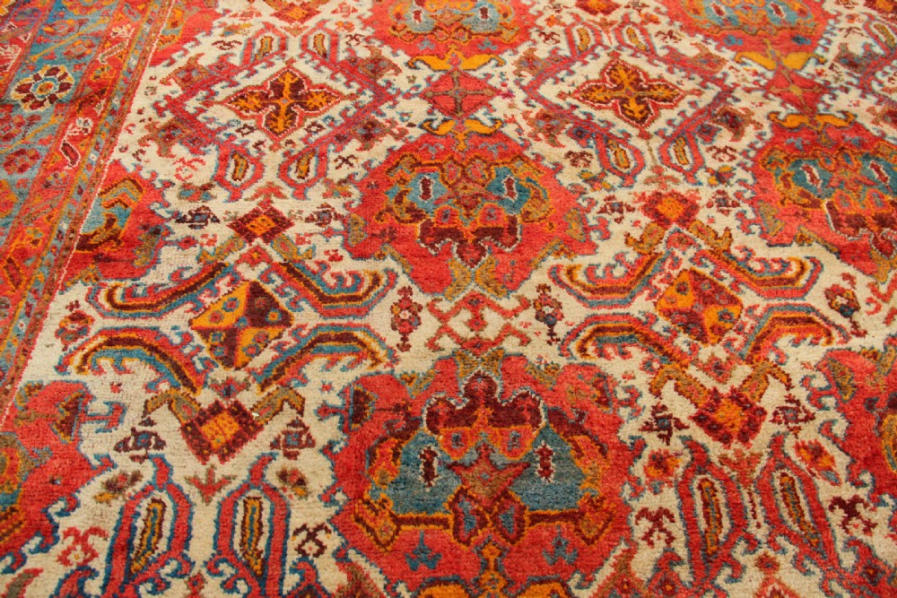 A large hand-knotted wool carpet featuring an ivory field decorated with geometric orange, terracotta, and turquoise medallion motifs within a wide multi-layered border. View VII