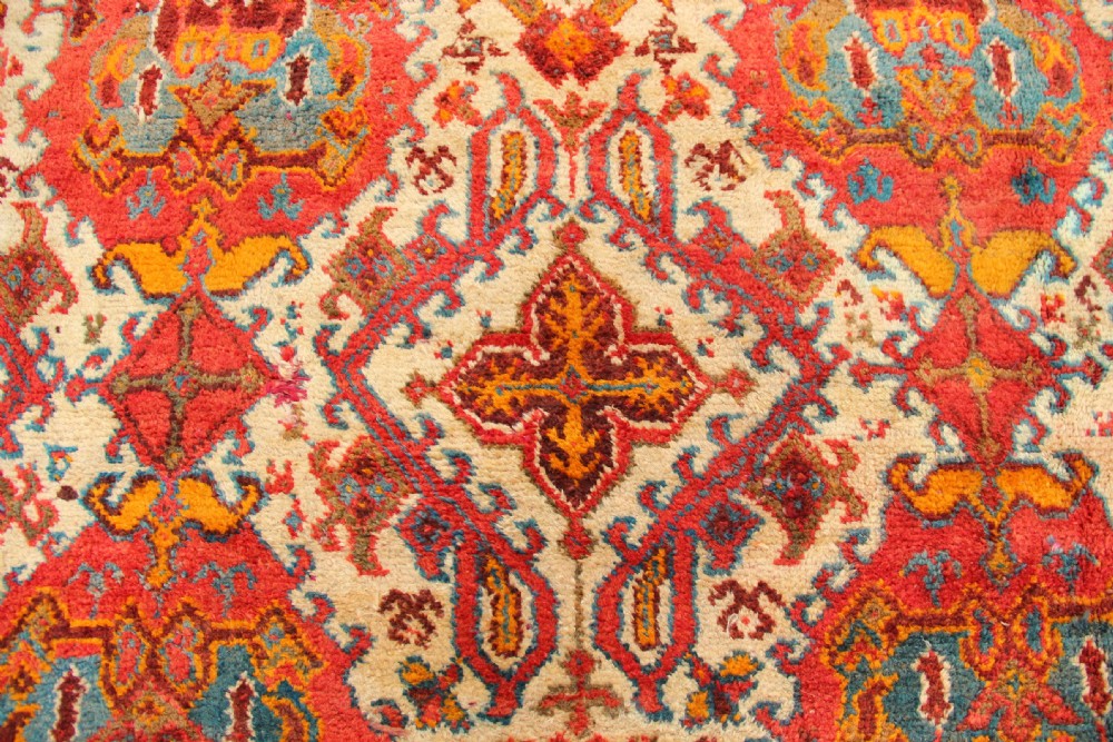 A large hand-knotted wool carpet featuring an ivory field decorated with geometric orange, terracotta, and turquoise medallion motifs within a wide multi-layered border. View VIII