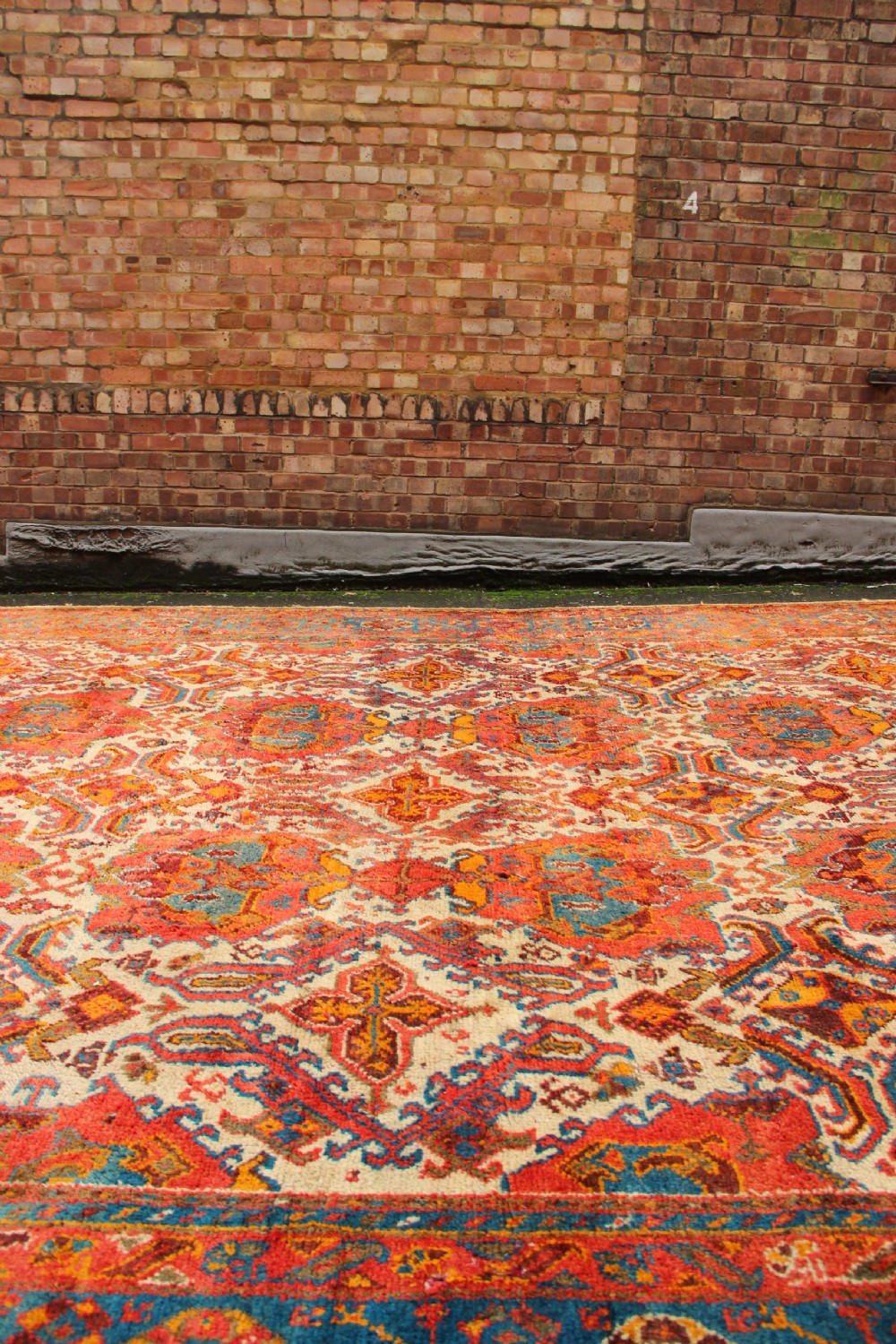 A large hand-knotted wool carpet featuring an ivory field decorated with geometric orange, terracotta, and turquoise medallion motifs within a wide multi-layered border. View X
