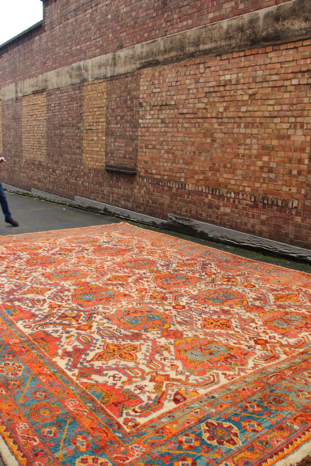 A large hand-knotted wool carpet featuring an ivory field decorated with geometric orange, terracotta, and turquoise medallion motifs within a wide multi-layered border. View XII