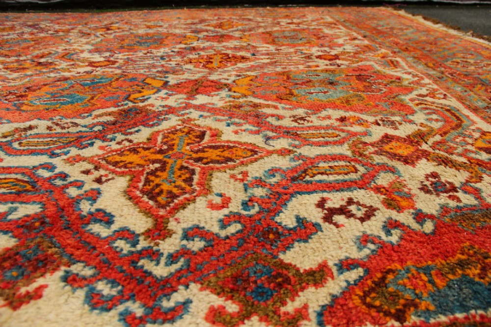 A large hand-knotted wool carpet featuring an ivory field decorated with geometric orange, terracotta, and turquoise medallion motifs within a wide multi-layered border. View XIV