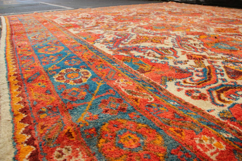 A large hand-knotted wool carpet featuring an ivory field decorated with geometric orange, terracotta, and turquoise medallion motifs within a wide multi-layered border. View XV