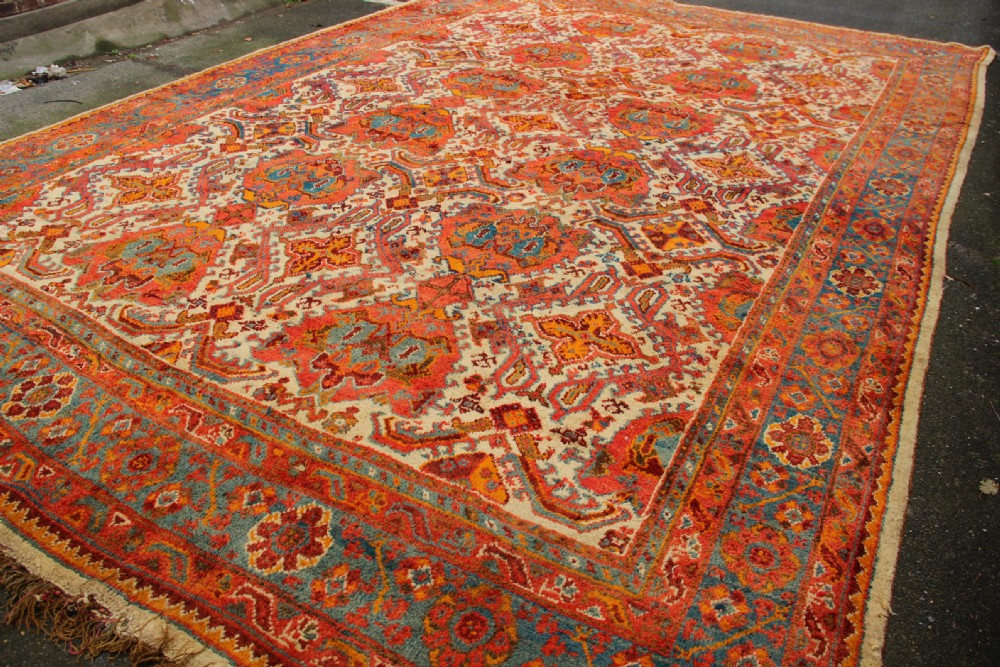 A large hand-knotted wool carpet featuring an ivory field decorated with geometric orange, terracotta, and turquoise medallion motifs within a wide multi-layered border. View XVI