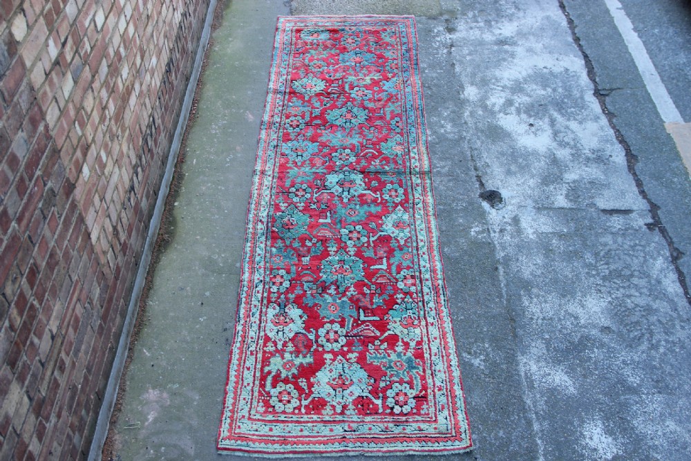 An elongated antique Oushak runner featuring an intricate floral pattern in shades of green and pink on a vibrant ground.