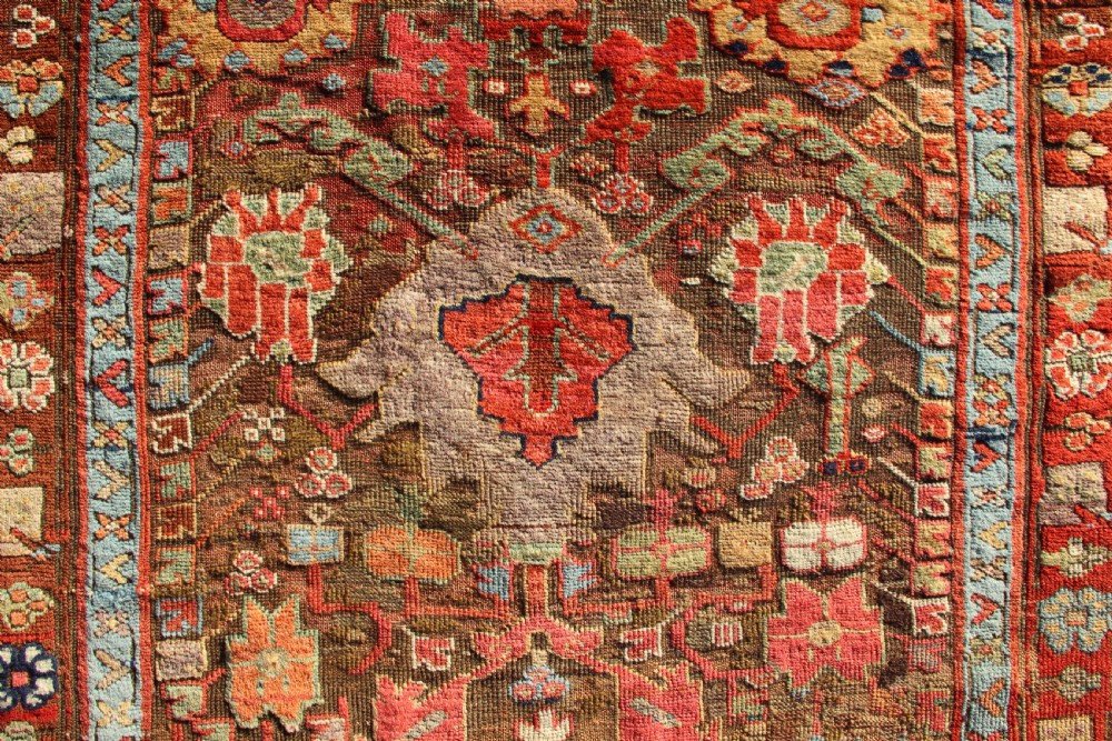 An early nineteenth-century hand-knotted wool Kurdish Sauj Bulagh rug with geometric tribal medallions in terracotta red, blue, and ochre yellow tones. View II