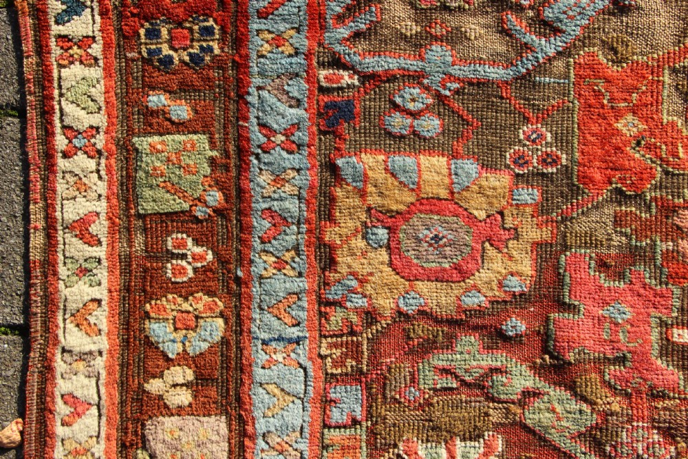 An early nineteenth-century hand-knotted wool Kurdish Sauj Bulagh rug with geometric tribal medallions in terracotta red, blue, and ochre yellow tones. View III
