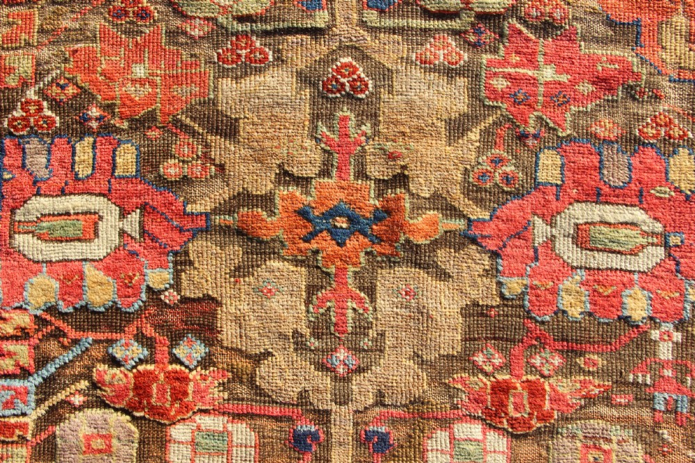 An early nineteenth-century hand-knotted wool Kurdish Sauj Bulagh rug with geometric tribal medallions in terracotta red, blue, and ochre yellow tones. View VI