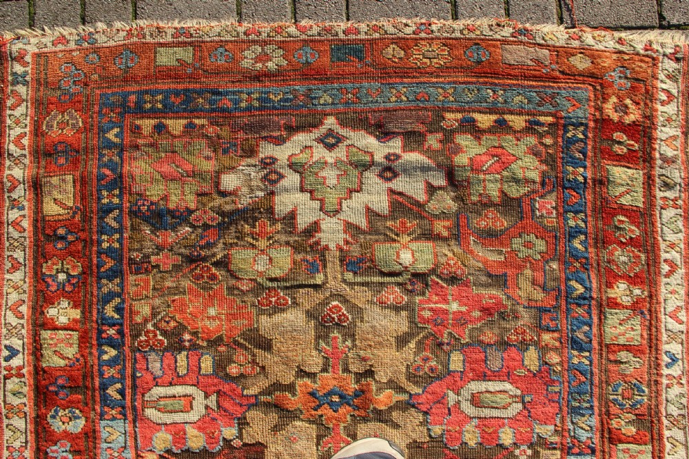 An early nineteenth-century hand-knotted wool Kurdish Sauj Bulagh rug with geometric tribal medallions in terracotta red, blue, and ochre yellow tones. View VII