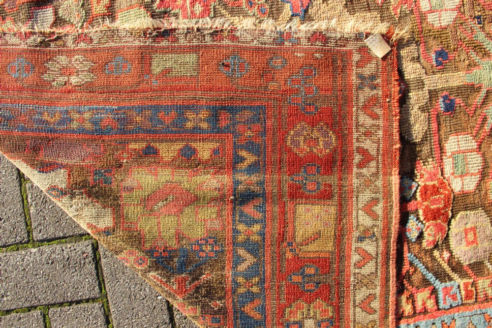 An early nineteenth-century hand-knotted wool Kurdish Sauj Bulagh rug with geometric tribal medallions in terracotta red, blue, and ochre yellow tones. View IX