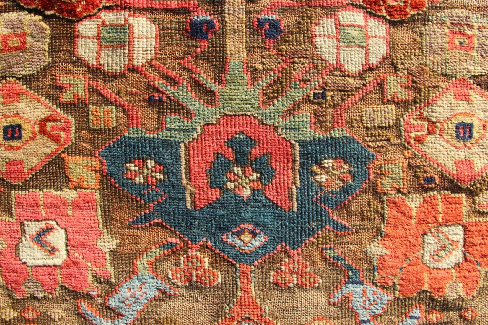 An early nineteenth-century hand-knotted wool Kurdish Sauj Bulagh rug with geometric tribal medallions in terracotta red, blue, and ochre yellow tones. View X