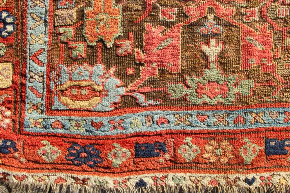 An early nineteenth-century hand-knotted wool Kurdish Sauj Bulagh rug with geometric tribal medallions in terracotta red, blue, and ochre yellow tones. View XI
