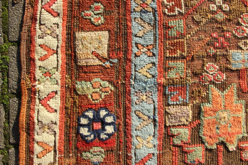 An early nineteenth-century hand-knotted wool Kurdish Sauj Bulagh rug with geometric tribal medallions in terracotta red, blue, and ochre yellow tones. View XII