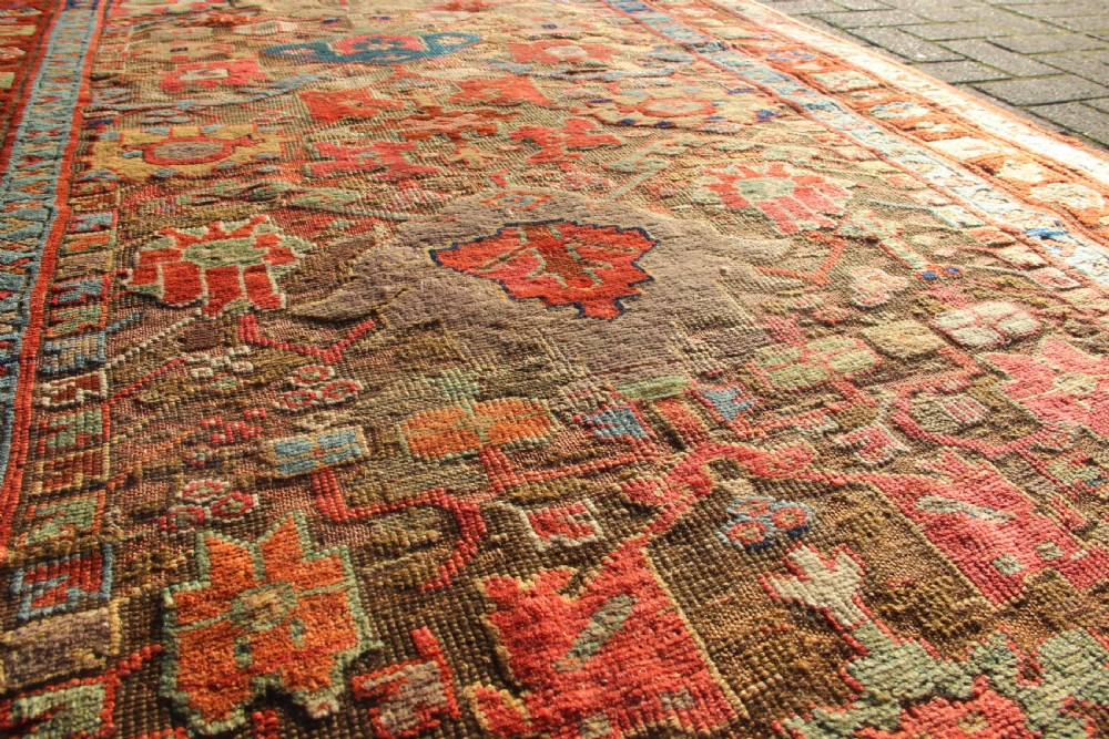 An early nineteenth-century hand-knotted wool Kurdish Sauj Bulagh rug with geometric tribal medallions in terracotta red, blue, and ochre yellow tones. View XIII