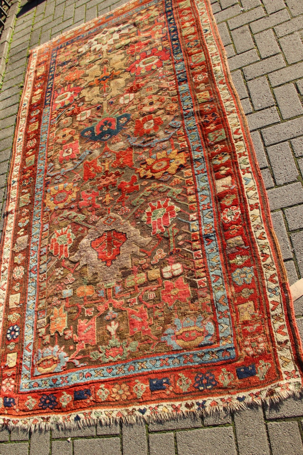 An early nineteenth-century hand-knotted wool Kurdish Sauj Bulagh rug with geometric tribal medallions in terracotta red, blue, and ochre yellow tones.