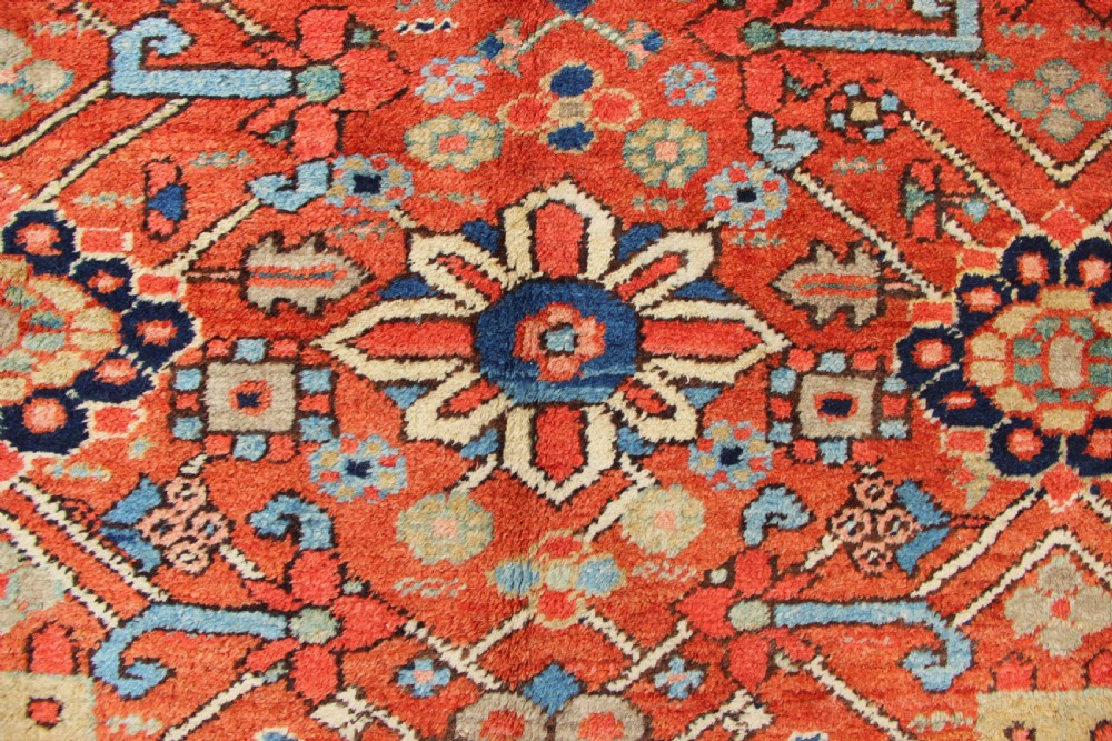 An antique Heriz wool carpet featuring a terracotta red field filled with geometric floral motifs framed by a navy blue border. View III