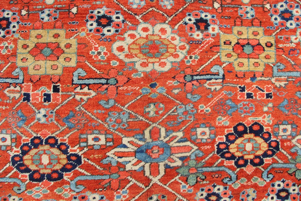 An antique Heriz wool carpet featuring a terracotta red field filled with geometric floral motifs framed by a navy blue border. View VI